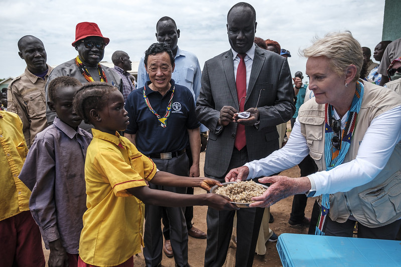 FAO/IFAD/WFP/Eduardo Soteras. Aweil, Sud Sudan- Direttrice Esecutiva WFP Cindy McCain porge un piatto di cibo ad uno studente durante una visita alla scuola elementare di Udhaba, nel villaggio di Udhaba, nell'ambito della visita ufficiale in Sud Sudan dei capi delle agenzie con sede a Roma.