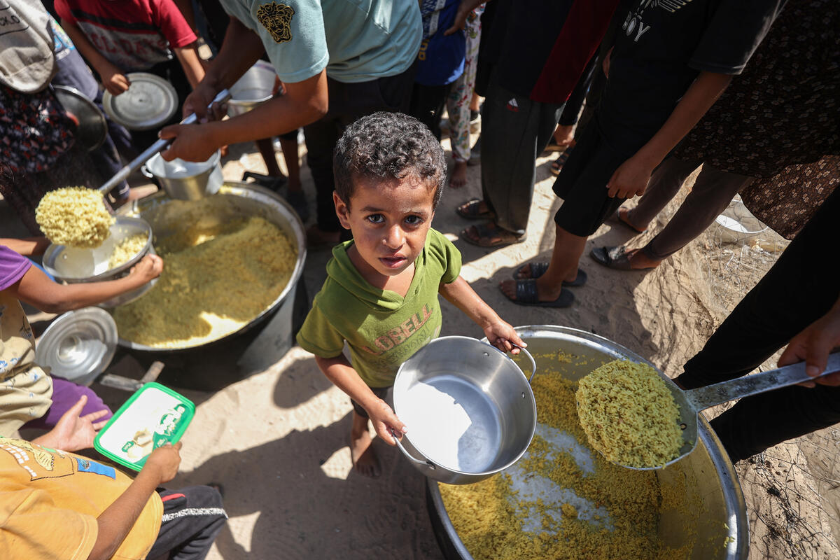 WFP/Ali Jadallah. Nella foto, i bambini ricevono e mangiano il riso che è stato portato da una vicina cucina per pasti caldi supportata dal WFP. I bambini aspettano pazientemente per ore questo pasto. In genere, lo portano poi alla tenda della famiglia. Gaza, Palestina.