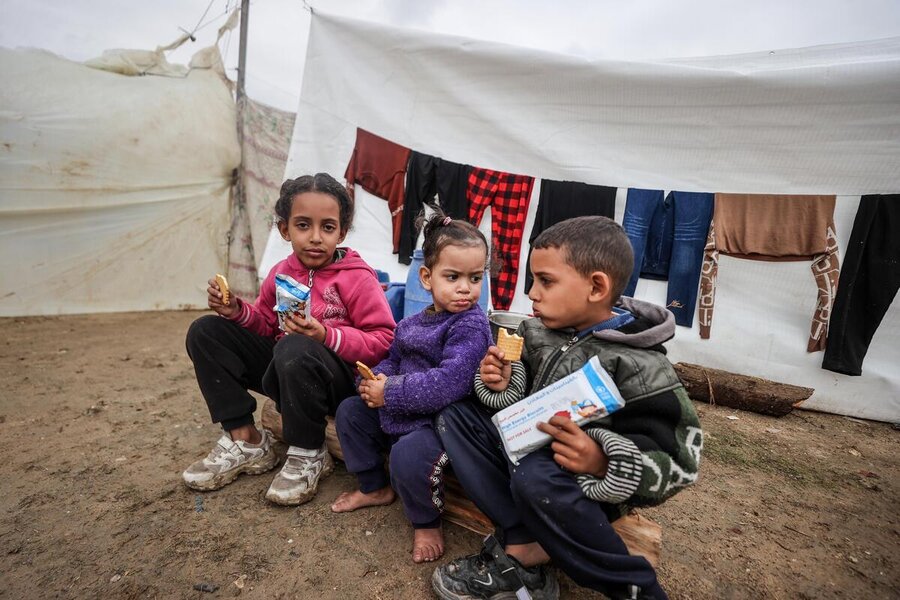 Gaza. Bambini seduti davanti a una tenda mangiano dei biscotti. 