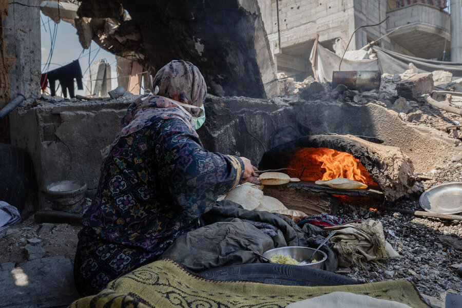 A makeshift street furnace burns as a person takes bread out in a destoryed environment