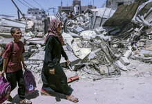 donna e bambino camminano tra case distrutte