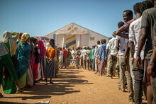 Due file di rifugiati, una di donne l'altra di uomini, davanti a un tendone dove si distribuiscono le razioni di cibo del WFP.